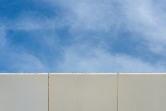 Abstract image, the corner of a modern building contrasting with the blue sky and soft white clouds.