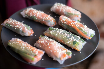 Raw spring rolls served on a black ceramic plate on wooden background, flat lay food photo, close up photo