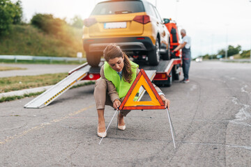 Middle age business woman after car accident putting safety or warning foldable triangle on the...