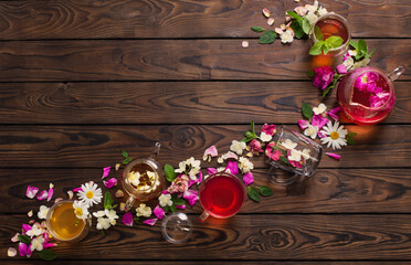 various teas with herbs and flowers on a dark wooden table, top view
