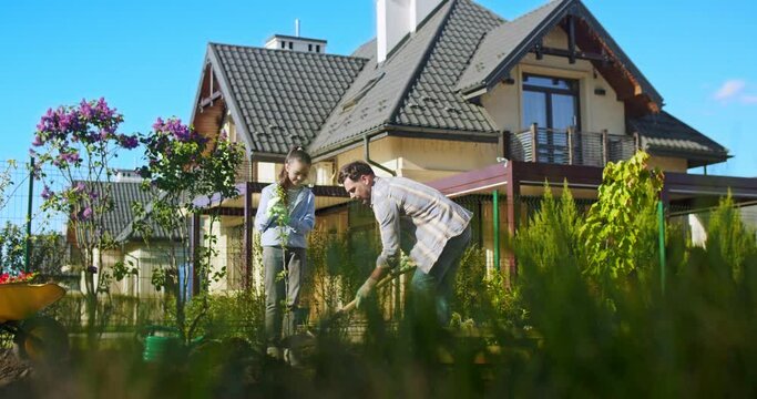 Happy joyful father and cute pretty daughter working in garden together and hugging to plant tree. Portrait shot. Little kid with dad planting trees in orchard. Outside.