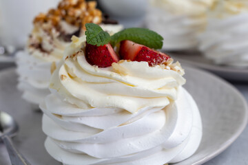 Pavlova meringue cakes with whipped cream and fresh strawberries, mint leaves. Selective focus.