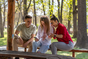 Young people watching online content in a smart phone sitting on a bench