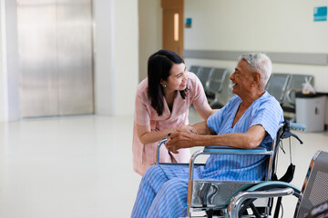 Asian elder male patient sitting on wheelchair. Woman doctor talk with senior patient at ceception...