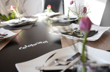 Modern laid table with pink tulip spring decoration and lettering „Celebrate!“ on a dark wooden table