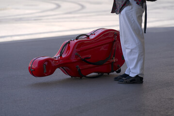 Red music instrument suitcase of cello at tram station Bellevue at City of Zürich on a sunny hot summer day. Photo taken June 19th, 2022, Zurich, Switzerland. © Michael Derrer Fuchs