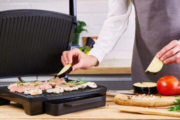 Female chef puts vegetables and eggplants on a wooden cutting board. Cooking in the home kitchen.