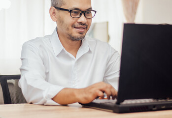 Happy man wearing glasses and smiling as he works on his black laptop where business is going well.