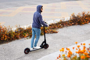 Bearded stylish man riding the electric scooter. Guy on daily commute riding micro scooter.
