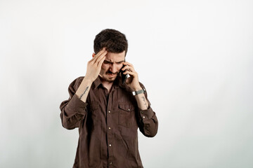 Happy young man wearing shirt posing isolated over white background feeling upset desperate talking on the phone having problems. Hearing bad news during mobile conversation.