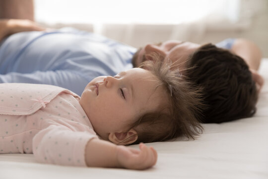 Close up calm newborn baby and young dad sleeping in bed, lying down with eyes closed looking carefree and peaceful resting together at home. Sweet dreams, protection, fatherhood, co-sleeping concept
