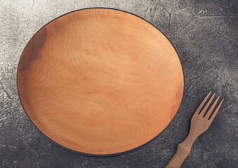 Wooden plate and fork lying on a textured gray table.