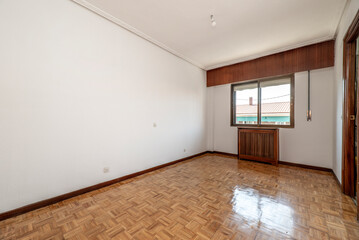Empty room with wooden radiator cover and lattice on the wall, aluminum window and oak parquet