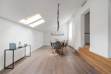 Natural wood dining table in the living room of an attic apartment with wooden steps and skylights...