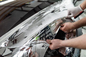 Car wrapping specialists putting silver mirror chrome foil on car. Selective focus.