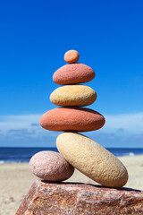 Rock zen pyramid of white and pink pebbles on a background of blue sky and sea.