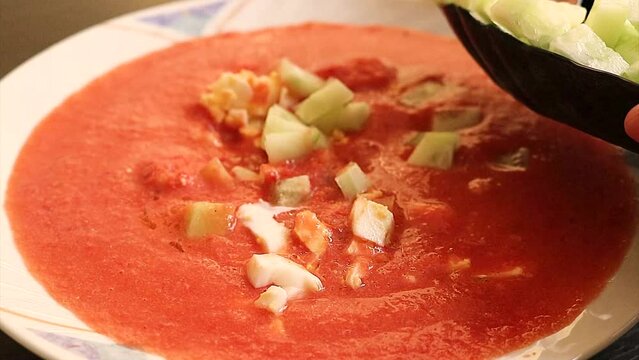 recipe of gazpacho from close up, adding cucumber dressing and boiled egg with a spoon to the healthy Spanish cold soup made with tomato, garlic, pepper and olive oil