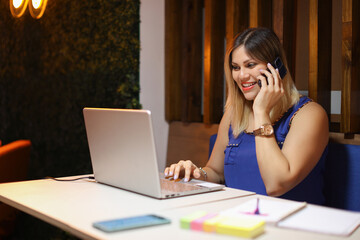 Entrepeneur woman talking on phone smiling with a laptop writing