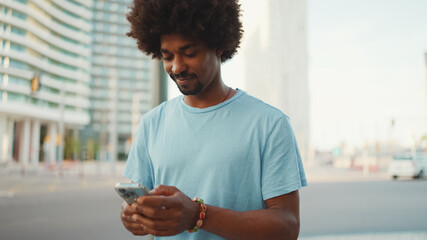 Closeup portrait of  young African American man in light blue t-shirt using his smartphone. Man...