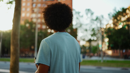 Close-up of young African American man in light blue t-shirt is standing on crosswalk. Back view