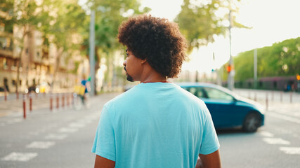 Close-up of young African American man in  light blue t-shirt is standing on crosswalk.