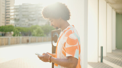 Closeup young African American man wearing shirt writes in social networks on mobile phone on urban...