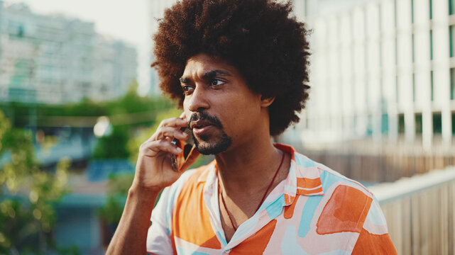 Close-up of young African American man wearing shirt walking and talking on smartphone. Lifestyle concept. Slow motion back lighting.