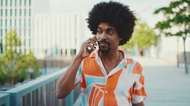 Close-up of young African American man wearing shirt walking and talking on smartphone. Lifestyle concept. Slow motion back lighting. - Powered by Adobe