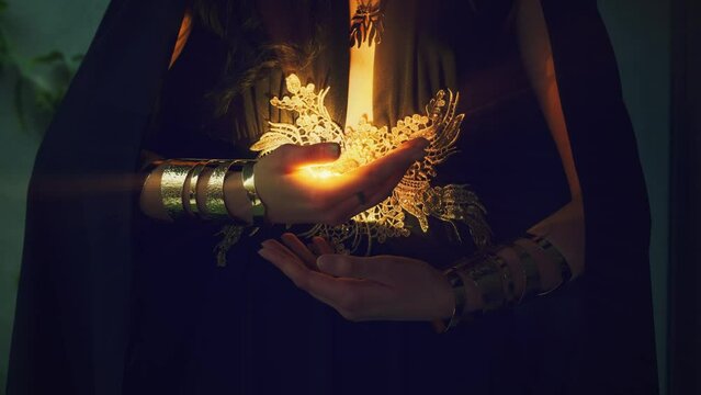 Mystery female hands close-up with magical light woman witch magician creates magic, casting spell bright shine in fingers. Halloween concept holiday party. Creative dark wizard costume, black dress