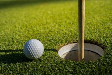 Gordijnen Choose focus. A white golf ball near the golf hole and a flagpole on green grass. © somchai