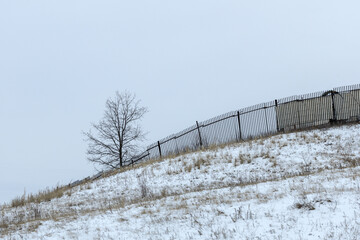 a sad landscape against a gray sky, snow and a crooked fence