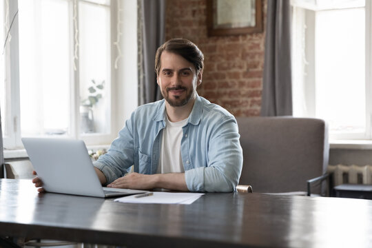 Successful ambitious entrepreneur, business owner portrait concept. Millennial man office employee posing look at camera sit at workplace desk, working on laptop, use modern tech, corporate software
