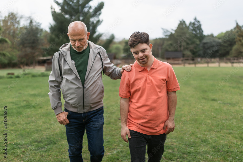 Wall mural happy senior father with his young son with down syndrome walking in park together.