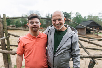 Happy senior father with his adult son with Down syndrome at ranch looking at camera.
