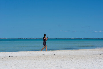 A young woman walks along the seashore looking at her smartphone at Isla Mujeres beach in Mexico