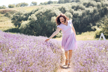 Fototapeta na wymiar Soft selective focus girl in purple dress walks on lavender field and enjoys the aroma of pink flowers and beauty on sunny day. Trendy color of 2022 Very peri. Digital detox pleasure of slow life.