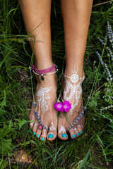 woman bare feet with mandala drawing  on grass with lot jewrly rings bracelets summer day close up