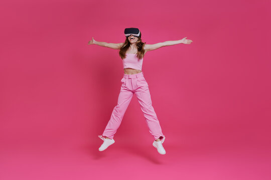 Full length of happy young woman in virtual reality headset jumping against pink background
