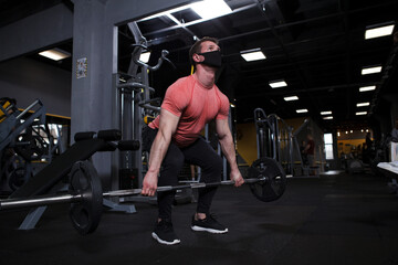 Fototapeta na wymiar Muscular male athlete wearing medical face mask, exercising with barbell at gym during pandemic