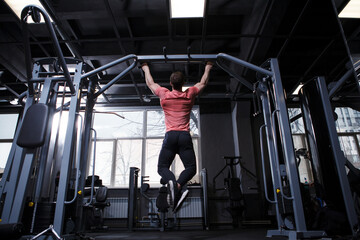 Rear view fulllength shot of an athletic muscular man doing pull-ups in crossover gym machine - obrazy, fototapety, plakaty