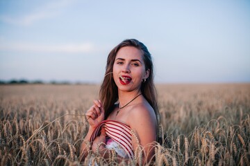 A young, slender, in black panties in a field of wheat covers her chest with a straw hat.