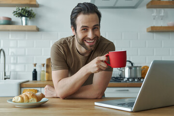 Cheerful man enjoying morning coffee while sitting at the kitchen island