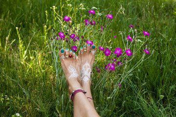 woman bare feet with mandala drawing  against flowers in field with rings and bracelets summer day...