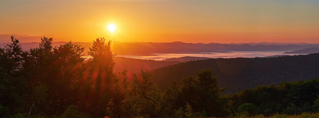Panorama of a beautiful sunrise in the mountains. White morning mist swirls in the valley