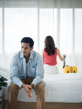 The anxiety of Asian couple lovers on the bed. Stressed man and young woman sitting on the bed with baggage wants to go away with relationship difficulties and feeling sad in the bedroom at home.