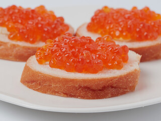 Naklejka na ściany i meble A red caviar sandwich on a plate on a white table