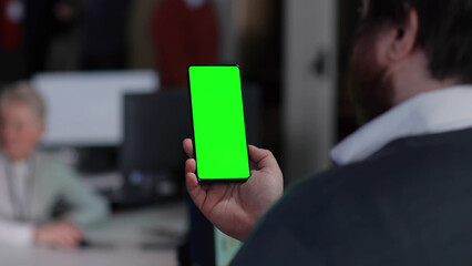 Back view of man looking at smartphone green screen in office