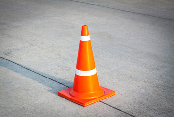 Striped orange cones on the asphalt road. Plastic orange cone on the road. Traffic cone on a parking lot in the park. traffic cone, with white and orange stripes on gray asphalt, copy space.