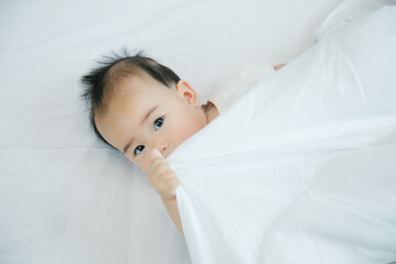 Cute little asian baby on bed with soft blanket indoors