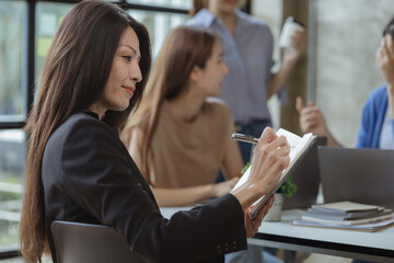Fototapeta premium Asian teenage women sit in a startup company meeting room, young generation co-found and develop a plan to grow and differentiate a startup company. Startup company development by new generation.